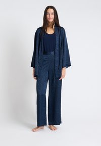 Marineblauw pyjama set met een kimono-stijl jas, voorzien van een bladerenpatroon in groen en blauw. Glad stof met wijde broekspijpen en korte mouwen.