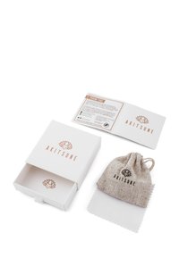 Cutie albă cu logo roz auriu, conținând un plic din material textil, o lavetă de curățare și un card de mulțumire. Plicul este bej și are șnur.