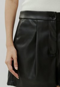Zwarte leren shorts met een gladde textuur, featuring een platte tailleband en een zijzak, geaccentueerd met een enkele knoopsluiting.