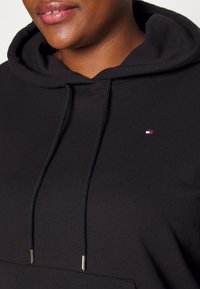 Sudadera negra con capucha y cordones, que presenta un pequeño logo bordado en rojo, blanco y azul en el pecho. Material suave de mezcla de algodón.