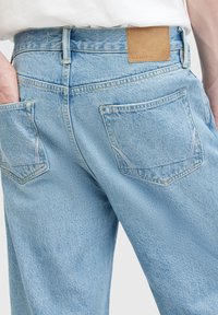 Los jeans de mezclilla azul claro cuentan con una cintura alta, bolsillos traseros con costuras curvas y una etiqueta de cuero marrón en la parte trasera.
