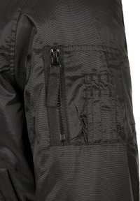Veste noire en nylon avec une poche zippée et un panneau en tissu texturé. Comprend une poche à rabat avec des accents de couture horizontale.