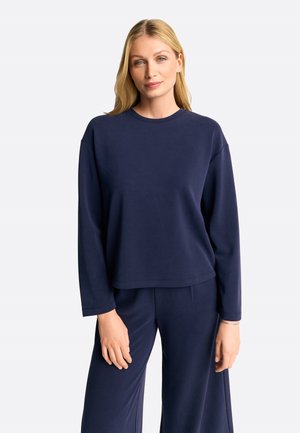 Felpa blu navy a maniche lunghe con scollatura rotonda e vestibilità rilassata, realizzata in tessuto morbido, abbinata a pantaloni coordinati.