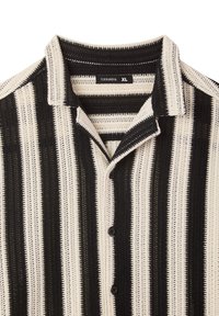 Camicia a maniche corte realizzata in tessuto testurizzato, caratterizzata da motivi a righe alternate bianche e nere, colletto e bottoni neri.