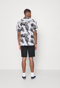 Short-sleeve shirt in white with black leaf print, paired with black shorts. Features a relaxed fit and a folded collar. Black sneakers worn.
