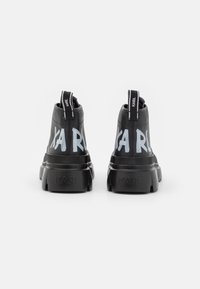 Par de zapatillas negras de caña alta con suelas gruesas, con letras blancas "KARL" en la parte posterior y tiradores de marca, sobre un fondo blanco.