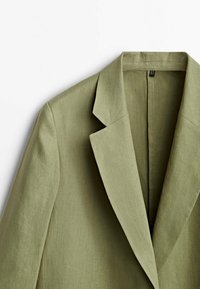Olijfgroen linnen blazer met een notch-kraag, gestructureerde schouders en een schoon, minimalistisch ontwerp. Gladde textuur, geen zichtbare hardware.