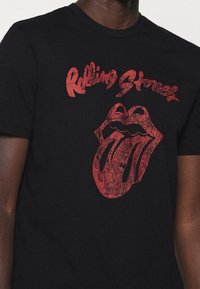 Czarna bawełniana koszulka z krótkim rękawem, z dekoltem typu crew neck, z zniszczonym czerwonym wzorem logo Rolling Stones i napisem.