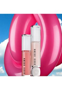 Due lip gloss Bobbi Brown: uno con tonalità pesca e uno trasparente, entrambi con contenitori trasparenti rettangolari, su uno sfondo rosa vivace.