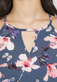 Top sans manches floral avec un fond marin, présentant des fleurs roses et violettes, des papillons, et un détail de décolleté en trou de serrure. Tissu doux et texturé.