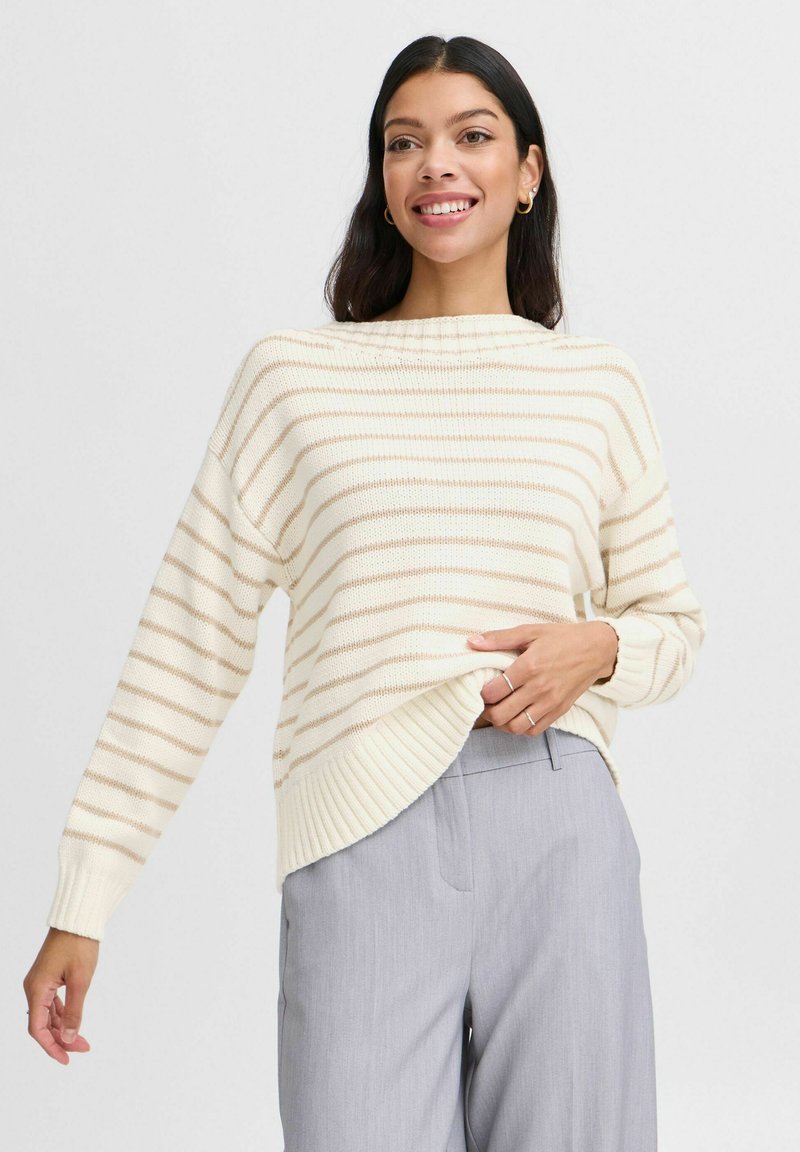 Cremestrickpullover mit beigen horizontalen Streifen, geripptem Saum und Bündchen, kombiniert mit hellgrauen Hosen. Weiche Stricktextur.