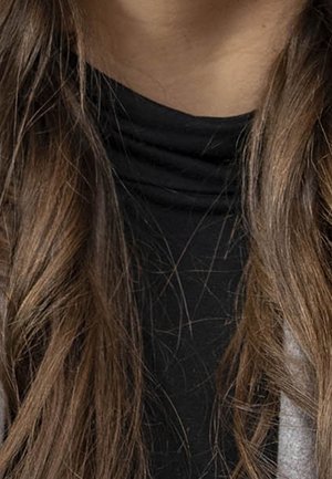Longs cheveux bruns sur un haut à col roulé noir et un vêtement extérieur clair, avec un focus sur le cou et la partie supérieure de la poitrine.