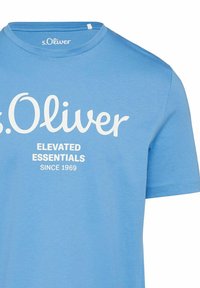 Light blue cotton t-shirt with short sleeves. Features a white printed logo and text reading "Elevated Essentials Since 1969" on the front.