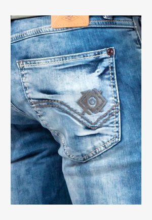 Light blue denim jeans featuring a back pocket with a decorative brown patch and stitched details in a wavy pattern.
