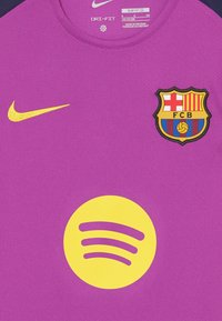 Violetinis Nike Dri-FIT marškinėliai su apvalia iškirpte. Ant krūtinės yra geltonas Spotify logotipas ir išsiuvinėtas FC Barcelona herbas.