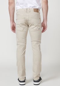 Vaqueros de mezclilla beige con corte recto, que cuentan con costuras en los bolsillos traseros y un parche de cuero marrón en la cinturilla. Combinados con zapatillas negras.