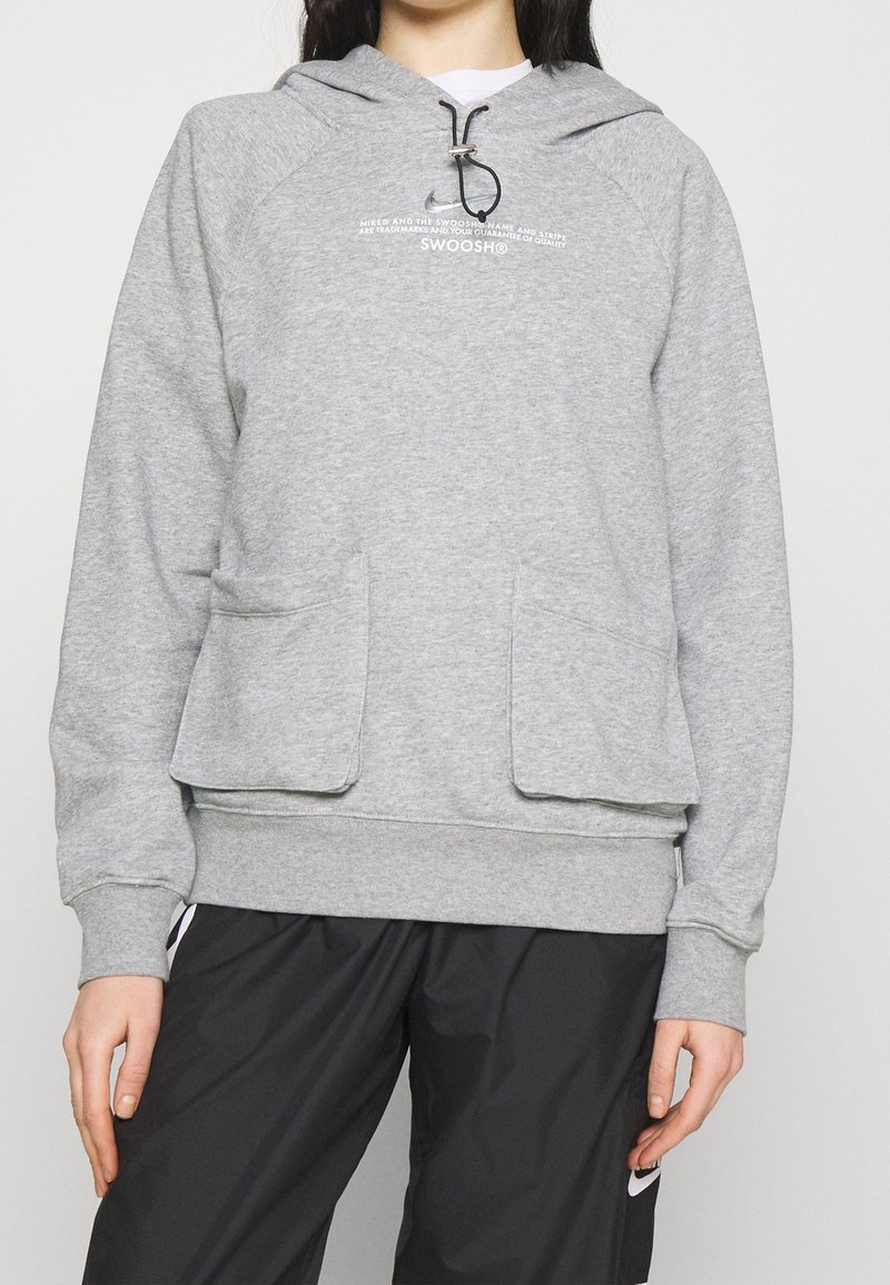 Grå hoodie gjord av mjukt tyg, med en framficka, dragsko på huvan och tryckt logotypdetalj på bröstet. Lämplig för avslappnad användning.