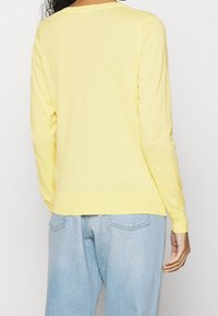 Gul långärmad tröja med rund hals och ribbad mudd. Mjuk tyg, figurnära stil, tillsammans med ljusblå jeans.