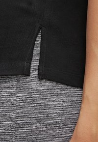 Chemise noire avec une fente latérale, associée à un tissu gris texturé. La chemise présente une texture lisse et légère, mettant en valeur le contraste avec le pantalon.