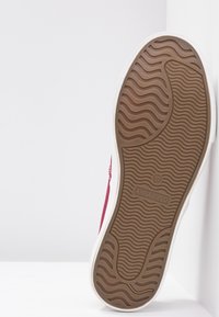 Sneaker in tessuto rosso con suola in gomma bianca. La suola presenta un motivo ondulato e all'interno sono visibili il logo e la taglia 37.