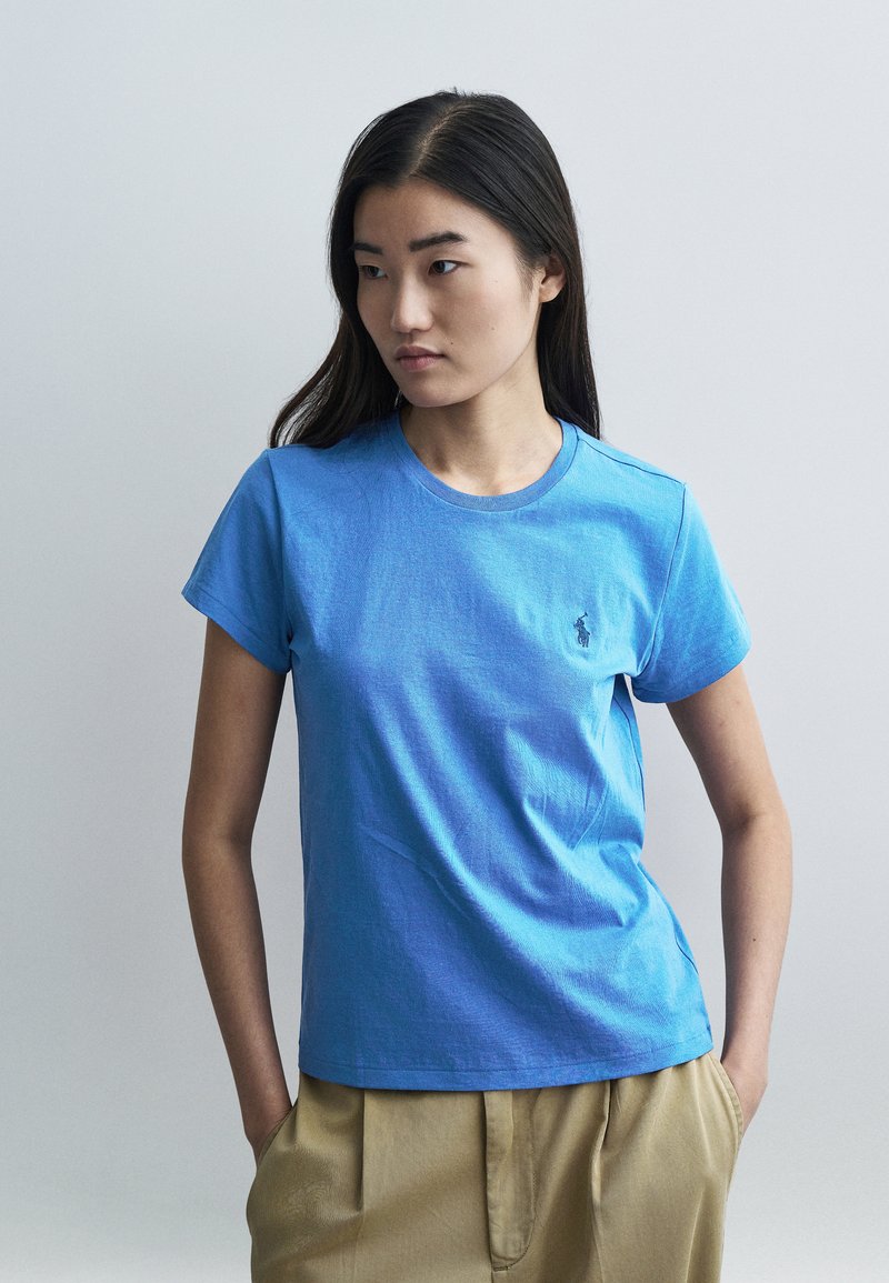 Kék pamut rövid ujjú póló, kerek nyakkivágással és apró hímzett logóval a bal mellrészen. Simap textúra, laza szabás.