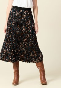 Zwarte geplooide rok met een bloemenpatroon in beige, teal en rood. Voorzien van een zwarte elastische tailleband, gedragen met bruine haklaarzen.