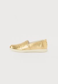 Gold metallic slip-on shoe with a rounded toe, featuring a smooth finish, elastic side panels, and a contrasting light-colored sole.