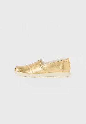 Scarpa slip-on metallica dorata con punta arrotondata, caratterizzata da una finitura liscia, pannelli elastici laterali e una suola di colore chiaro a contrasto.