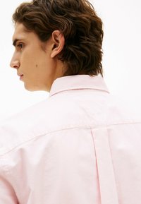 Jasnoróżowa koszula zapinana na guziki z klasycznym kołnierzykiem, szwem na plecach oraz jedną plisą, wykonana z gładkiej bawełnianej tkaniny.