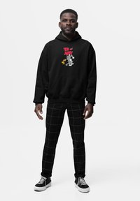 Hoodie nera con grafica "TOM and JERRY" che presenta i personaggi dei cartoni animati. Abbinata a pantaloni a quadri bianchi e neri e scarpe da ginnastica nere.