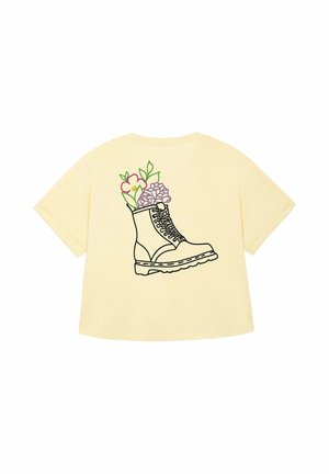 Geel T-shirt met een afbeelding van een zwarte laars gevuld met kleurrijke bloemen, met roze en paarse bloemen naast groene bladeren.