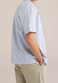 Ljusblå kortärmad skjorta med vertikala vita ränder, knappad krage, strukturvävt tyg och en avslappnad passform, kombinerad med beiga byxor.