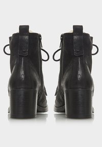 Botas de cuero negro hasta el tobillo con puntera redonda, tacón ancho medio, cremalleras laterales y embellishments decorativos de lazos en la parte trasera. Textura suave.