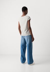 Camicia a maniche corte a righe in bianco e beige, abbinata a pantaloni in denim blu a vestibilità comoda. Sneakers bianche semplici, hardware minimal, senza accenti visibili.