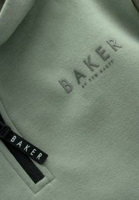 Zelená mikina s texturovaným povrchem. Na hrudi se nachází embosované logo "BAKER" a černý zip s štítkem s nápisem "BAKER."