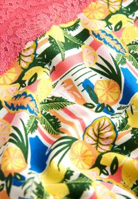 Színes szövet citrusfélékkel, trópusi levelekkel és rózsaszín csipkés szegéllyel, sima, csíkos háttéren.