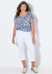 Top corto de mangas cortas con patrón de conchas en azul marino y blanco, combinado con pantalones cropped blancos y zuecos plateados. Textura suave, diseño casual, ajuste relajado.
