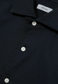 Diepblauwe shirt van textuurstof met een button-down kraag en witte knopen, met een REISS-label op de binnenkant van de kraag.