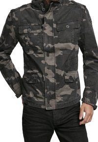 Kamouflagejacka i nyanser av grått och svart, med dragkedja fram, två bröstfickor, knappdetaljer och huva. Tillverkad av strukturerad tyg.