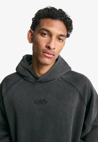 Charcoal gray hoodie with a soft texture, featuring a kangaroo pocket and a stitched logo on the chest. Designed with a relaxed fit and oversized hood.