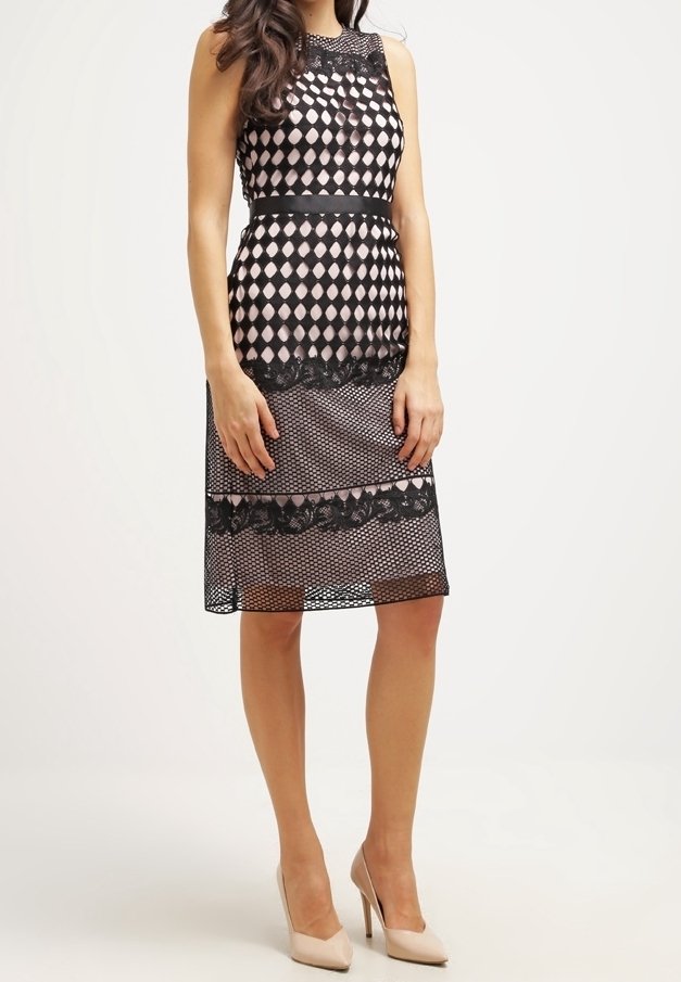 Czarna koronkowa sukienka z diamentowym wzorem, dopasowana góra i falbaniasty dół, z przezroczystą warstwą i satynowym paskiem w talii. Uzupełniona beżowymi szpilkami.