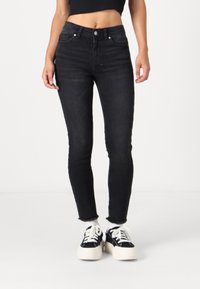 Fekete, skinny farmernadrág, magas derékkal, öt zsebes kialakítással és bolyhos szegéllyel. Fekete-fehér tornacipővel viselve.