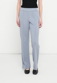 Lysegrå bukser med høj talje, elastisk taljebånd, lige ben og midter-pressede folder, kombineret med sorte flade sko.