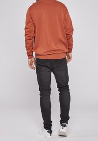 Herrtröja i orange med ribbade ärmslut, kombinerad med svarta slim-fit jeans och vita sneakers. Enkel design med slät textur.