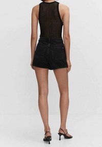 Shorts de mezclilla negra de talle alto con dobladillos deshilachados y dos bolsillos traseros, combinados con una camiseta sin mangas de tejido acanalado negra.