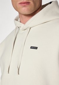 Hoodie gemaakt van zachte, lichte crème stof. Heeft een klein zwart Under Armour logo-opdruk en een trekkoord bij de hals.