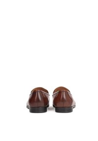Mocasines de cuero marrón con un acabado suave, puntera redondeada y costuras mínimas. Diseño clásico con un pequeño tacón flexible.