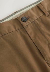 Pruunid, kerge kangaga lühikesed püksid, millel on lame esikülg, üksik must nööp ja kontrastse sisemise vöökoha vooder.