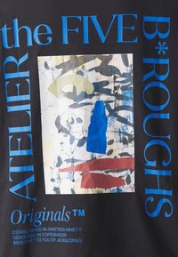 Μαύρο μπλουζάκι φτιαγμένο από ύφασμα με μια πολύχρωμη αφηρημένη γραφική εκτύπωση που περιλαμβάνει μπλε, πράσινα, κόκκινα και γκρι στοιχεία, καθώς και έντονο κείμενο σε μπλε και λευκό χρώμα.