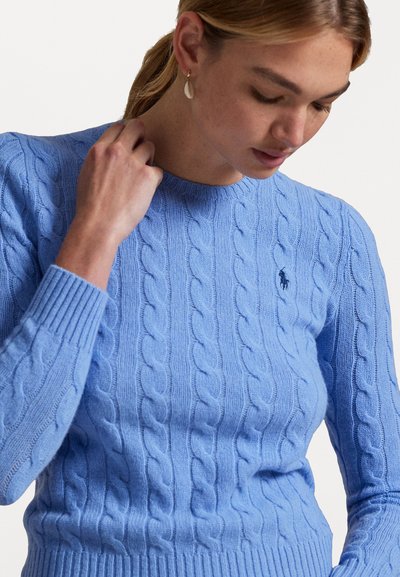Šviesiai mėlynas megztinis su kabelių raštu, apvali kaklo iškirptė ir banguoti rankogaliai. Maža logotipo detalė ant krūtinės suteikia subtilumo. Minkšta tekstūra.